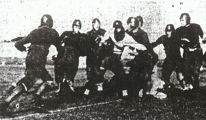 Alfred Ritchey (white jersey) is surrounded by gang of St. Augustine players in Cavemen's 6-02 victory.